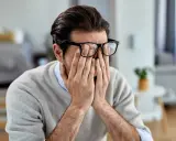 Mann mit Brille reibt sich die Augen, wirkt gestresst. Manche glauben, rauchen hilft gegen Stress, doch das ist ein Trugschluss.