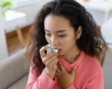 Junge Frau mit Asthma benutzt ihren Inhalator, der Cortison enthält, um ihre Atemwege zu öffnen.