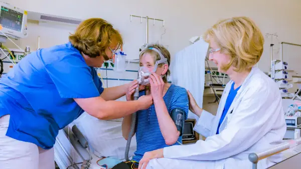 Ärztin und Pflegekraft helfen Patientin mit Lungenemphysem bei der Anpassung einer Beatmungsmaske. Medikamente sind Teil der Behandlung.