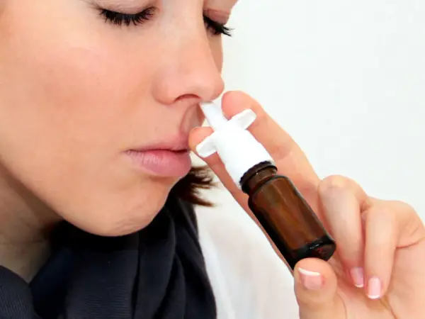 Frau mit geschlossenen Augen benutzt Nasenspray. Möglicherweise ein Test für eine Schimmelallergie.