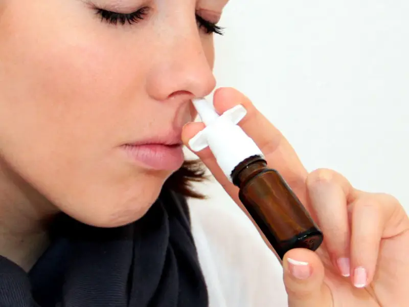 Frau mit geschlossenen Augen benutzt Nasenspray. Möglicherweise ein Test für eine Schimmelallergie.